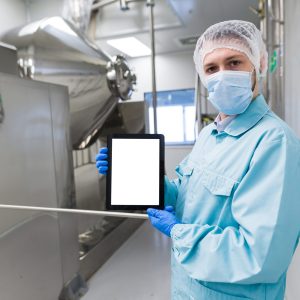 tablet on front, med worker in lab suit and gas mask showing empty tablet near steerl machine